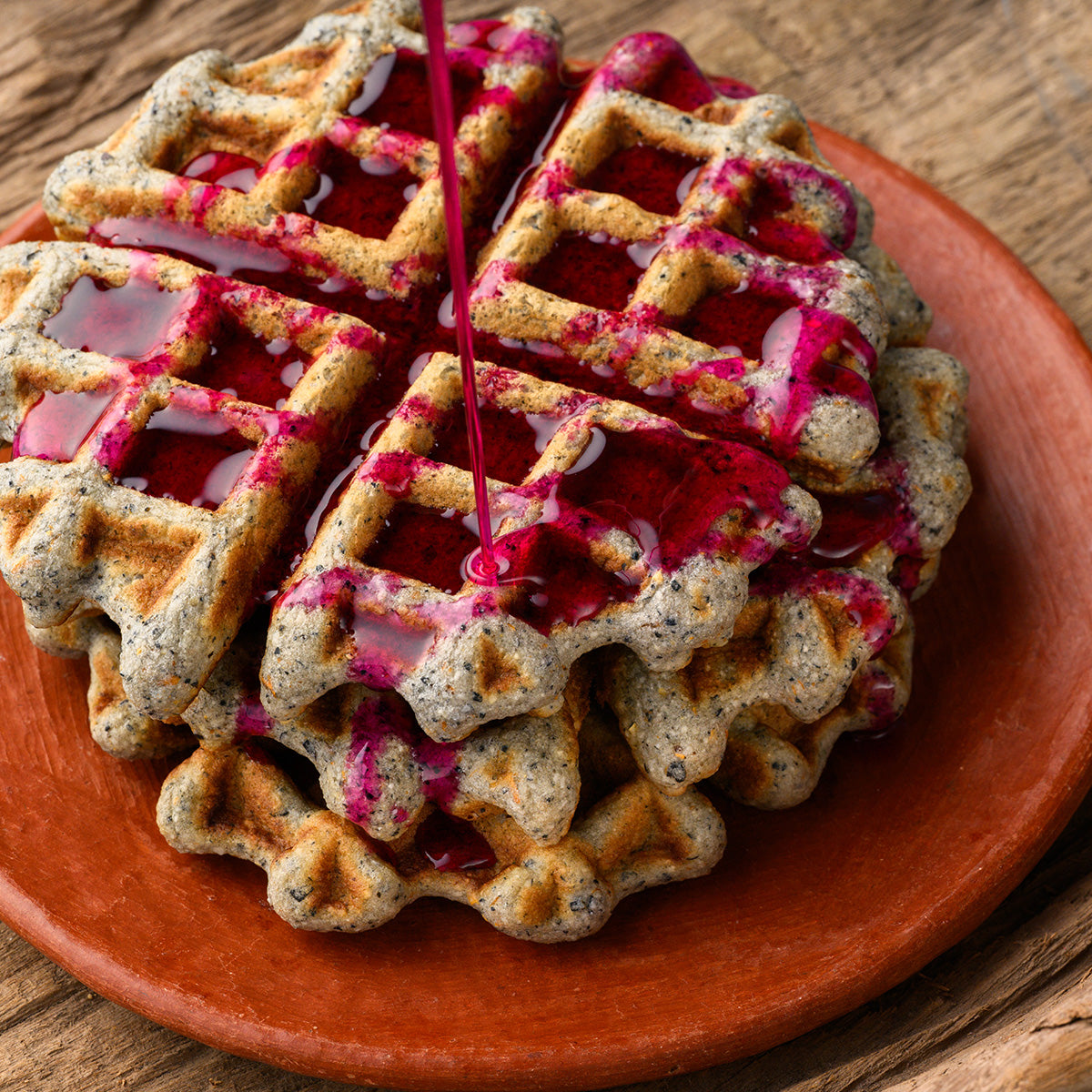 bluecorn waffle with pink prickly pear syrup being poured on top